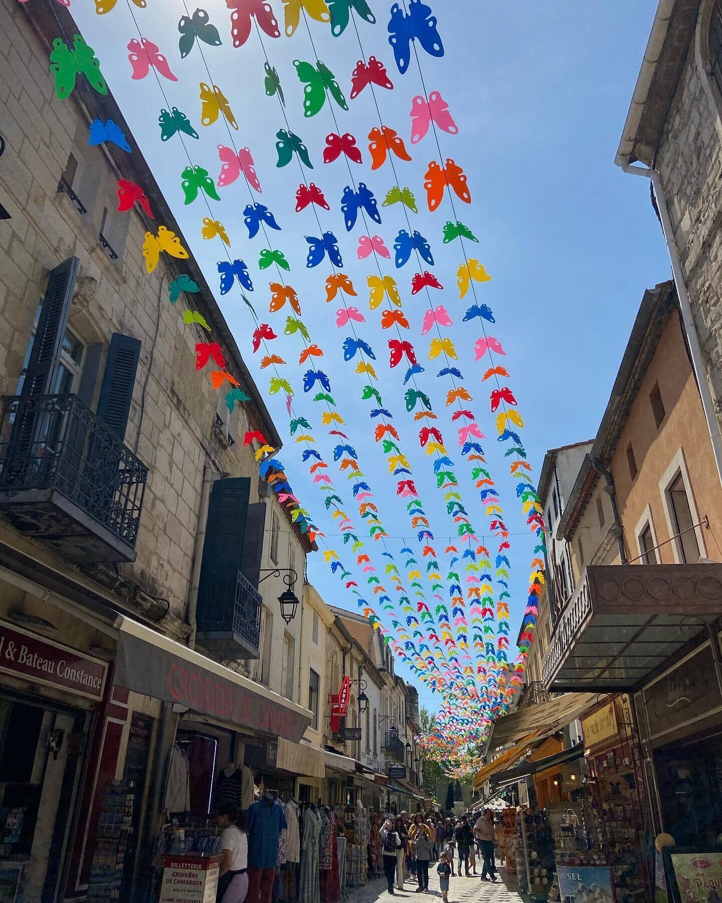 A street lined with shops and a colorful canopy of hanging paper butterflies.