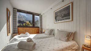 A bedroom with two beds, a large window with a view of mountains, and a zebra painting on the wall.