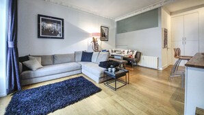 A modern living room with a sofa, coffee table, and a blue rug. There is a dining area with a table and chairs.