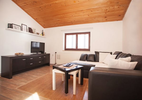 A modern living room with a wooden ceiling, a black sofa, a white table, and a TV on a black stand.
