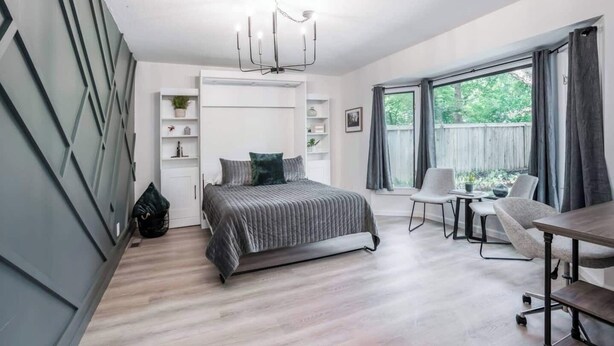 Et moderne soveværelse med seng, skrivebord og stol, med et stort vindue og en lysekrone.