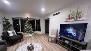 En moderne stue med et stort fladskærms-tv, et marmorbord, et juletræ og et hyggeligt siddeområde.