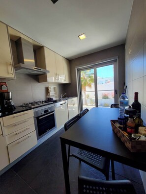 A modern kitchen with a gas stove, oven, and built-in cabinets. There is a dining table with chairs and a window with a view of palm trees.