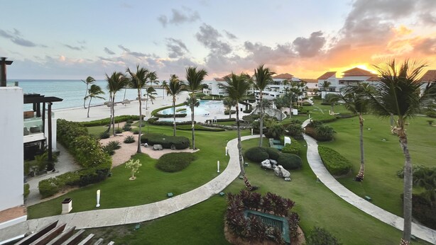 Ein Resort mit Pool, Palmen und Blick auf den Ozean bei Sonnenuntergang.