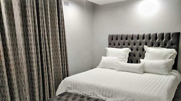 Ein Schlafzimmer mit einer gesteppten Kopfteil, einem großen Bett mit weißer Bettwäsche und einer grauen Sitzbank.