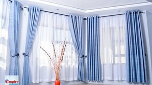 Ein Zimmer mit großen Fenstern, blauen und weißen Vorhängen und einer Vase mit Zweigen.