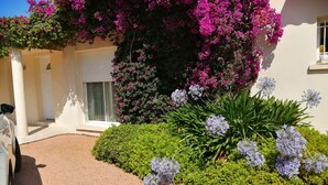 A building with a white facade, a covered entrance, and a garden with pink bougainvillea and purple flowers. - Comfortable villa overlooking the Gulf of Ajaccio  (Grosseto-Prugna)