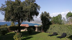 A grassy outdoor area with two lounge chairs, a tree, and a view of the sea and distant buildings. - Comfortable villa overlooking the Gulf of Ajaccio  (Grosseto-Prugna)