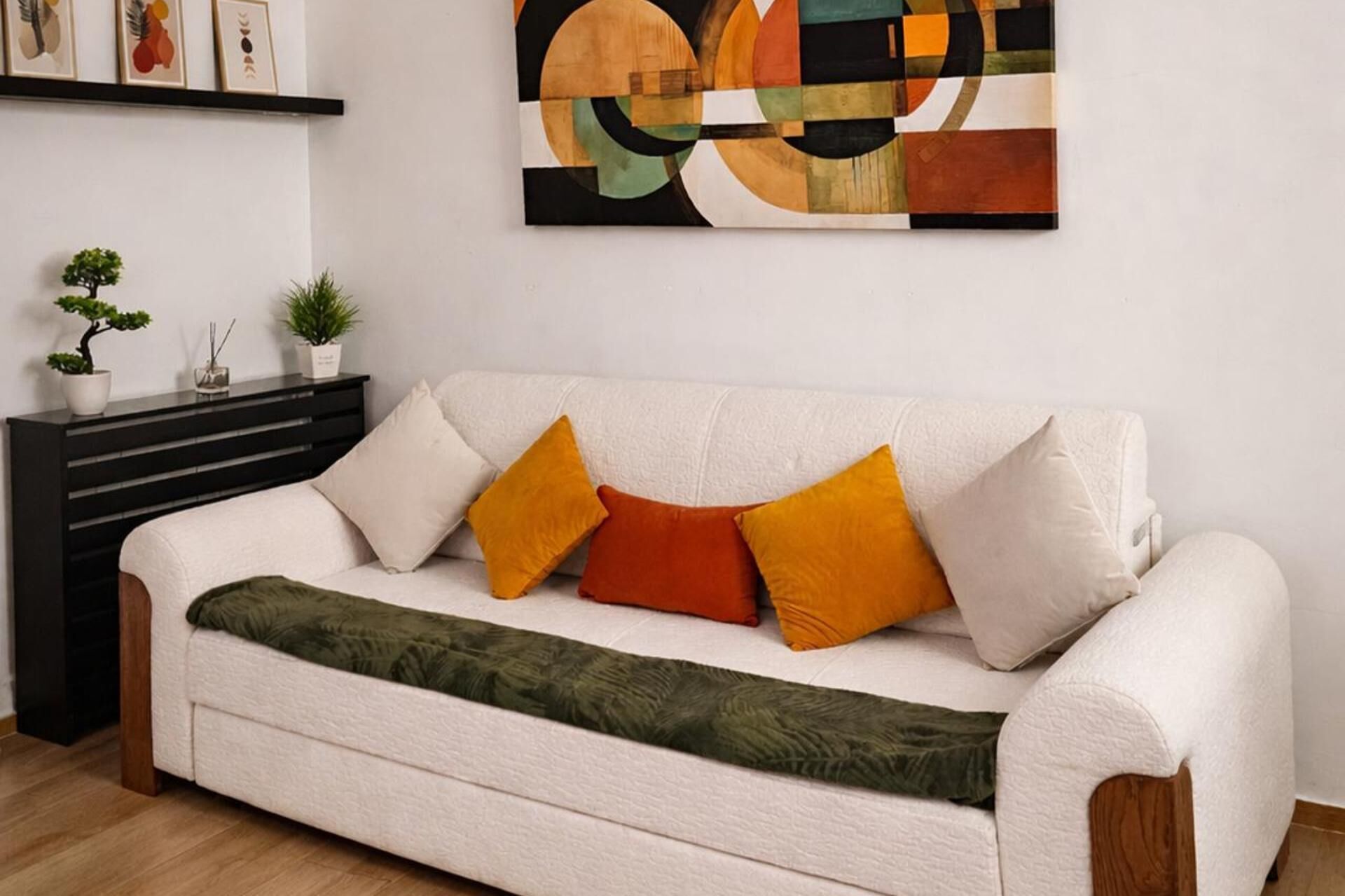 Un sofá blanco con varios cojines, una manta verde y una pared con arte abstracto.