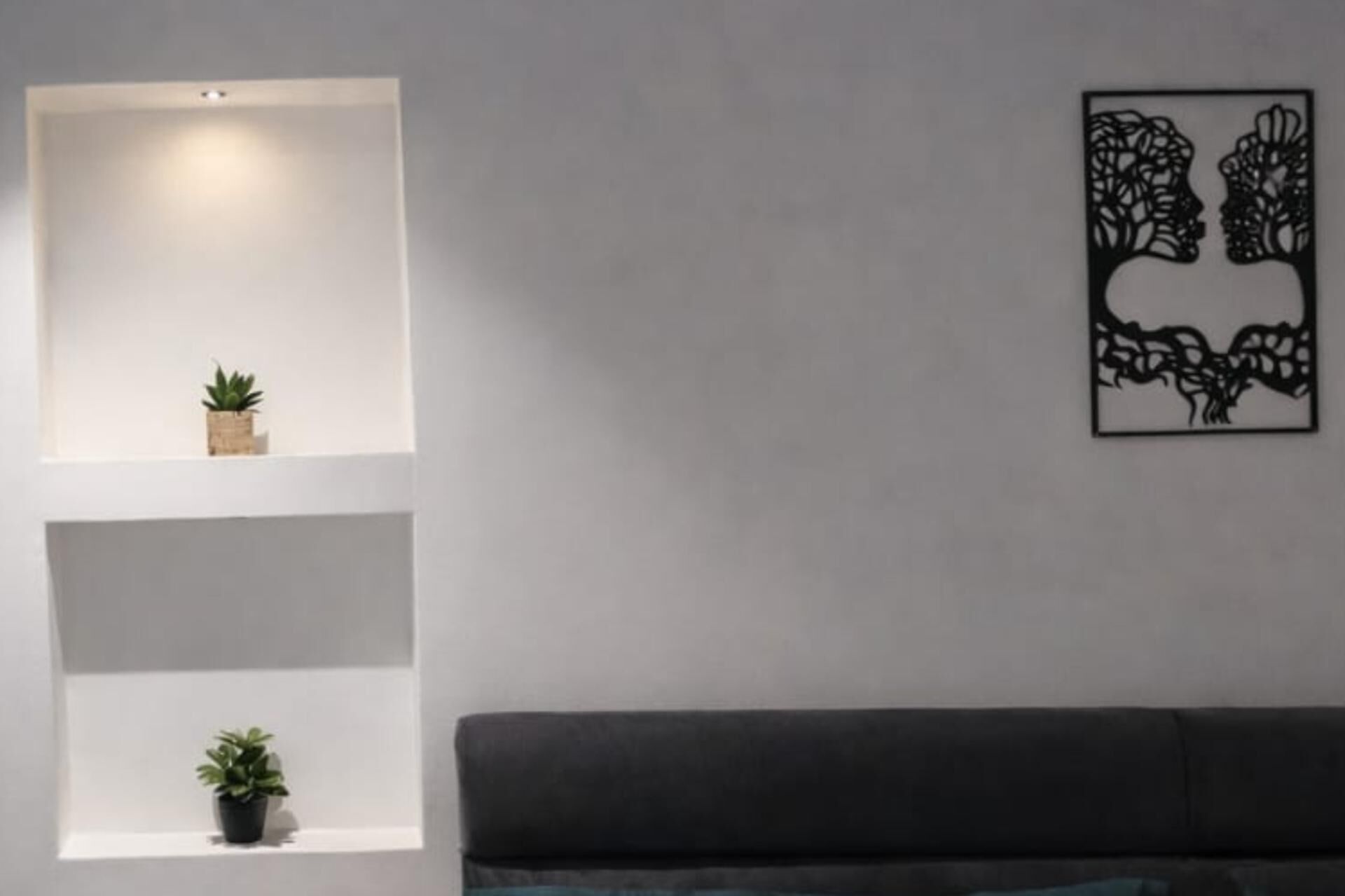 Un salon moderne avec un canapé foncé, des étagères blanches et une œuvre d’art abstraite accrochée au mur.