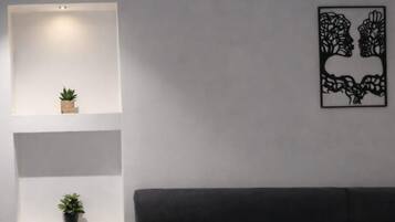Un salon moderne avec un canapé foncé, des étagères blanches et une œuvre d’art abstraite accrochée au mur.