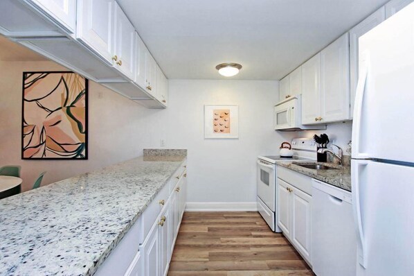 A compact kitchen with white cabinets, granite countertops, and a wooden floor. - South Seas Beach Villa 2414 (Captiva)