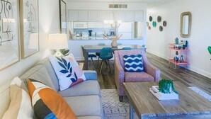 A living room with a sofa, armchairs, a coffee table, and a dining area with a table and chairs. There is a kitchen in the background with cabinets and appliances. - South Seas Beach Villa 2414 (Captiva)