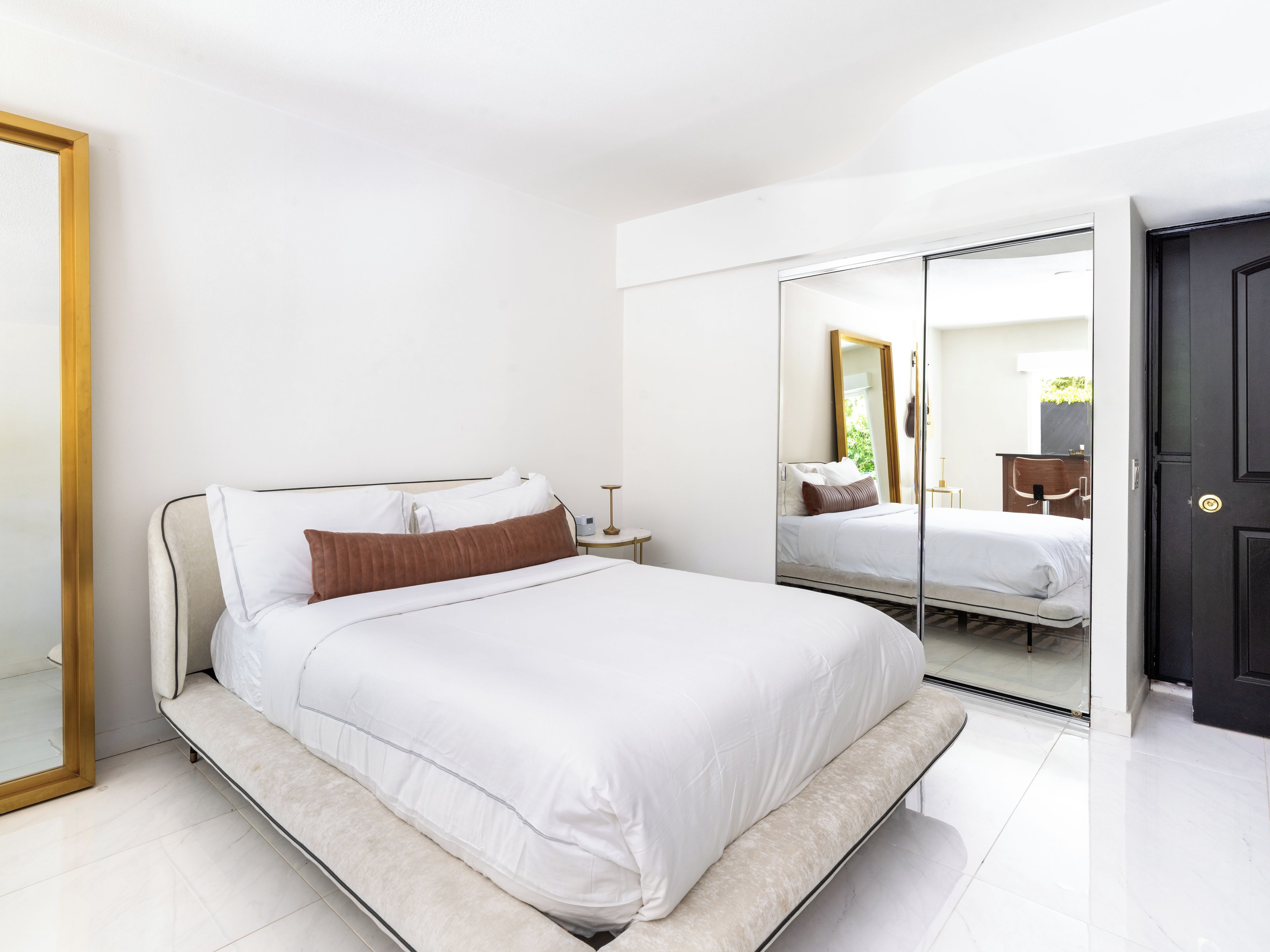 A modern bedroom with a bed, bedside table, and a large mirror.