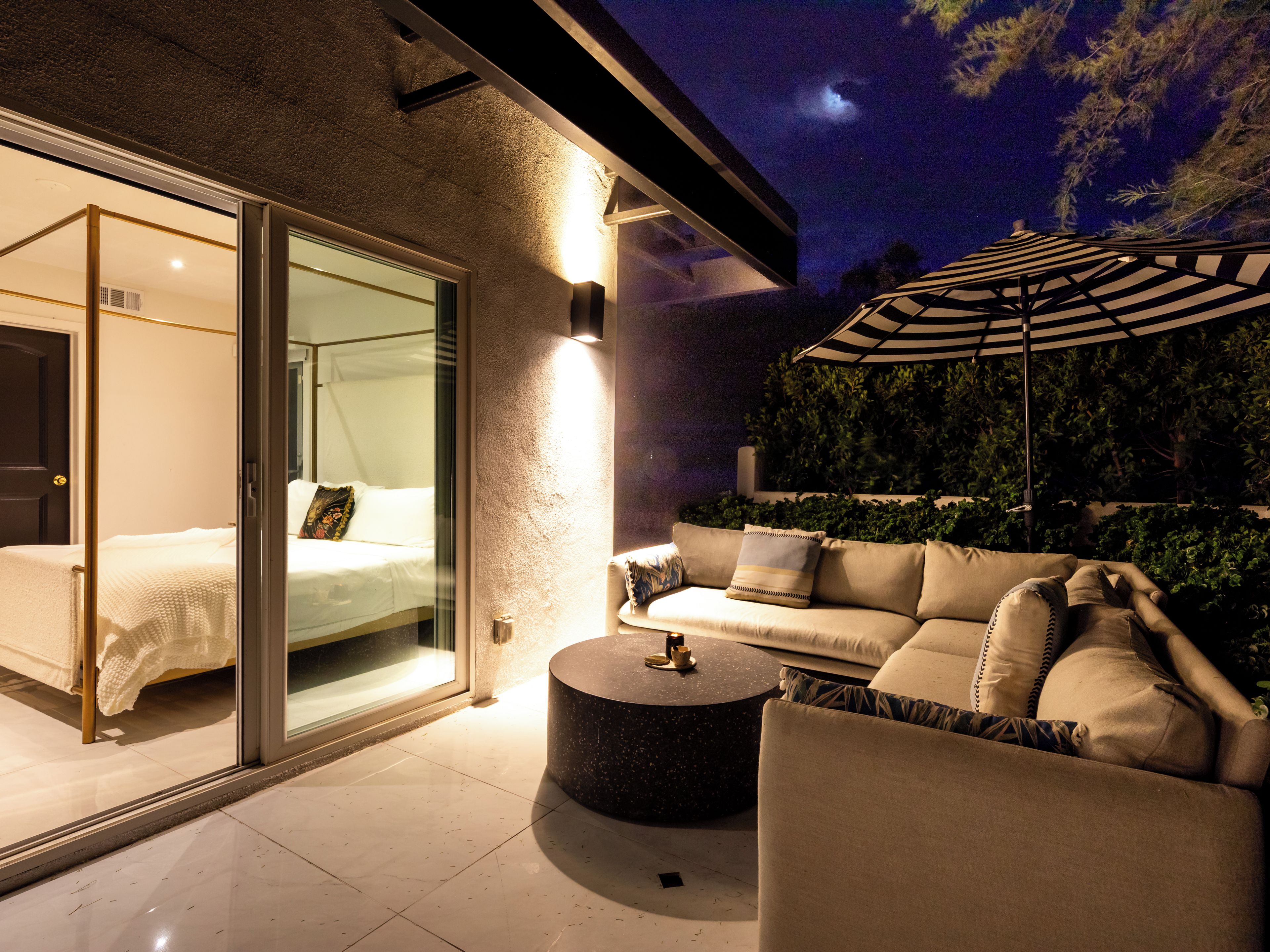 A modern outdoor living area with a sofa, a round coffee table, and a glass door leading to a bedroom.