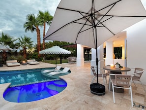 A pool area with lounge chairs, a table, and umbrellas.