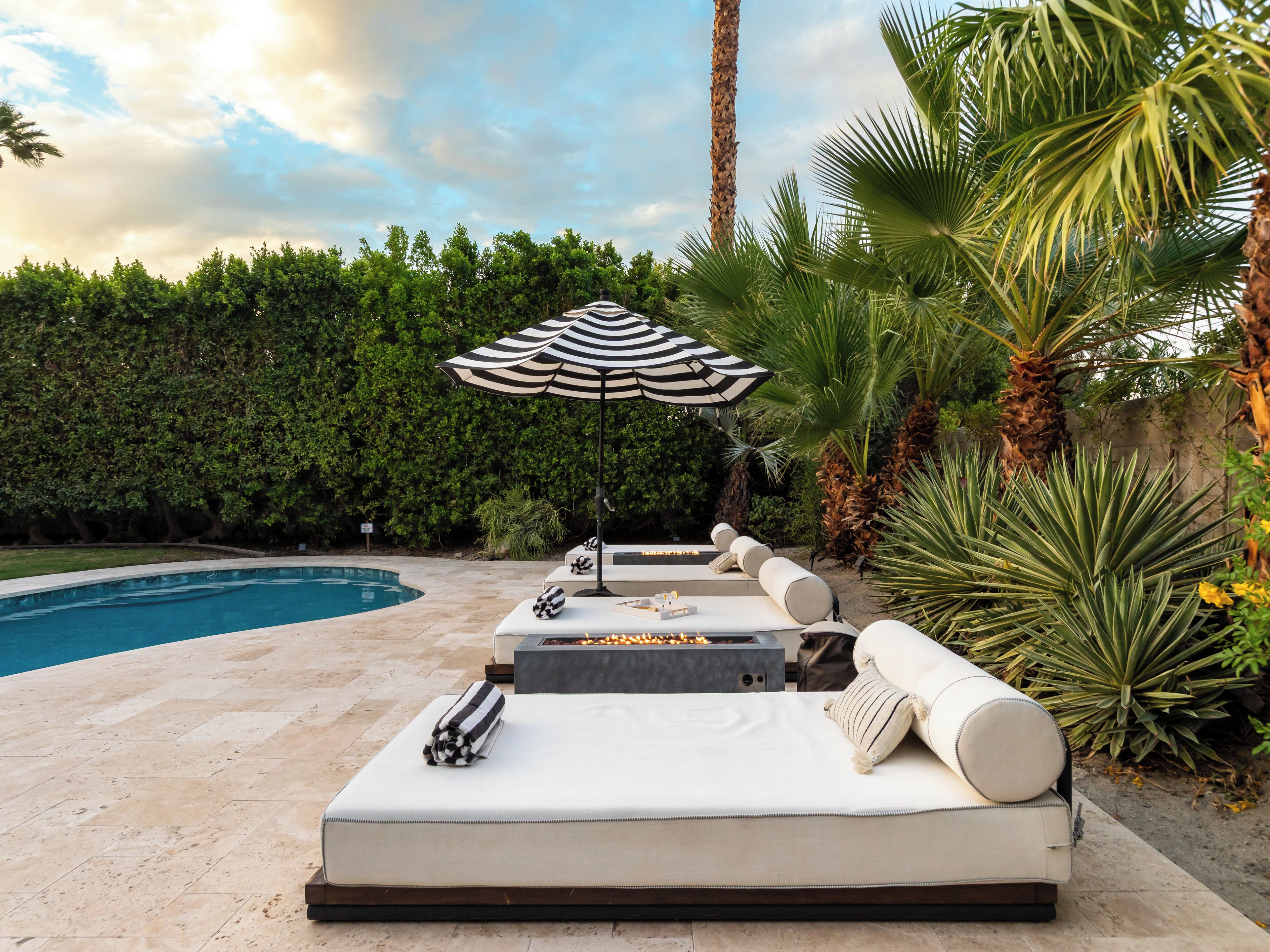 A poolside lounge area with a sofa, an umbrella, and a fire pit.