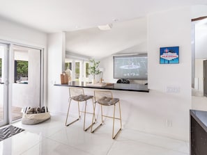 A modern kitchen with a bar area, two chairs, a potted plant, and a welcome sign.