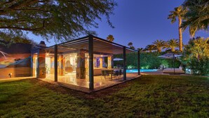 Ein moderner Außenbereich mit Terrasse, Glasveranda, Schwimmbad und Palmen.