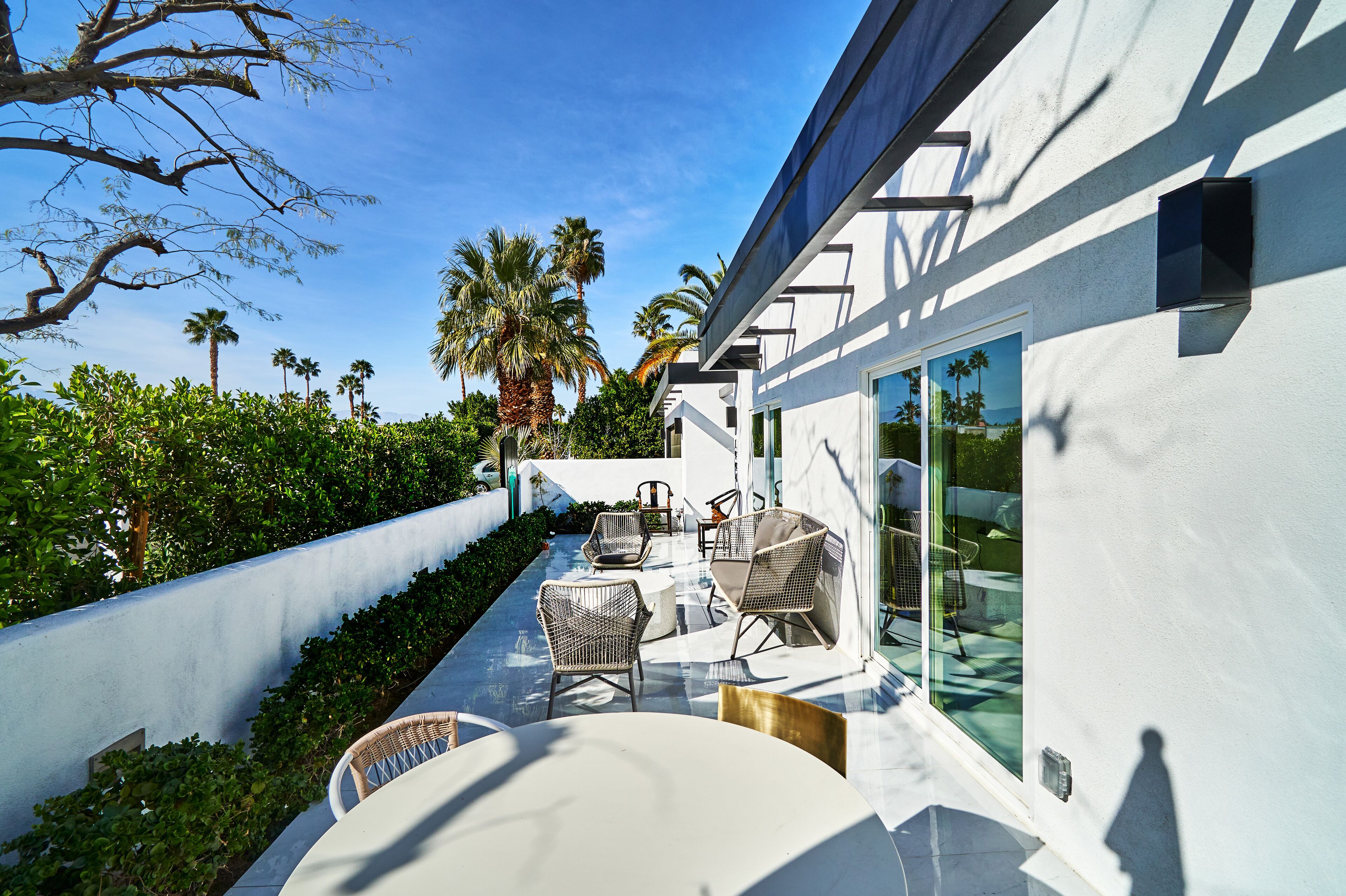 A modern outdoor patio with wicker furniture, a glass door leading to a pool, and a view of palm trees and the ocean.