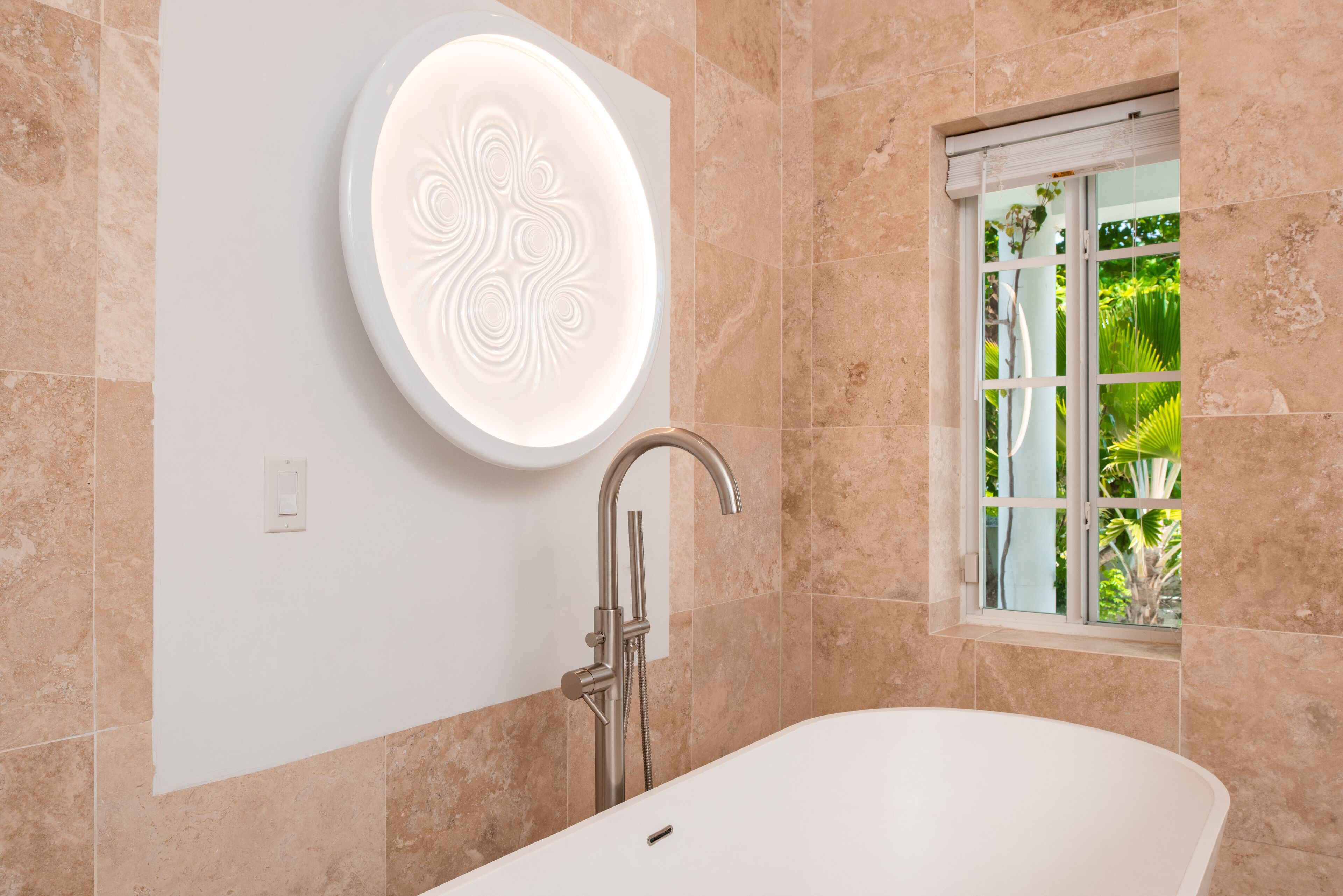 A modern bathroom with a freestanding bathtub, a wall-mounted vanity, and a window with a view of greenery.