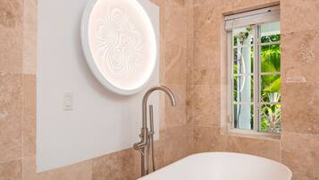 A modern bathroom with a freestanding bathtub, a wall-mounted vanity, and a window with a view of greenery.
