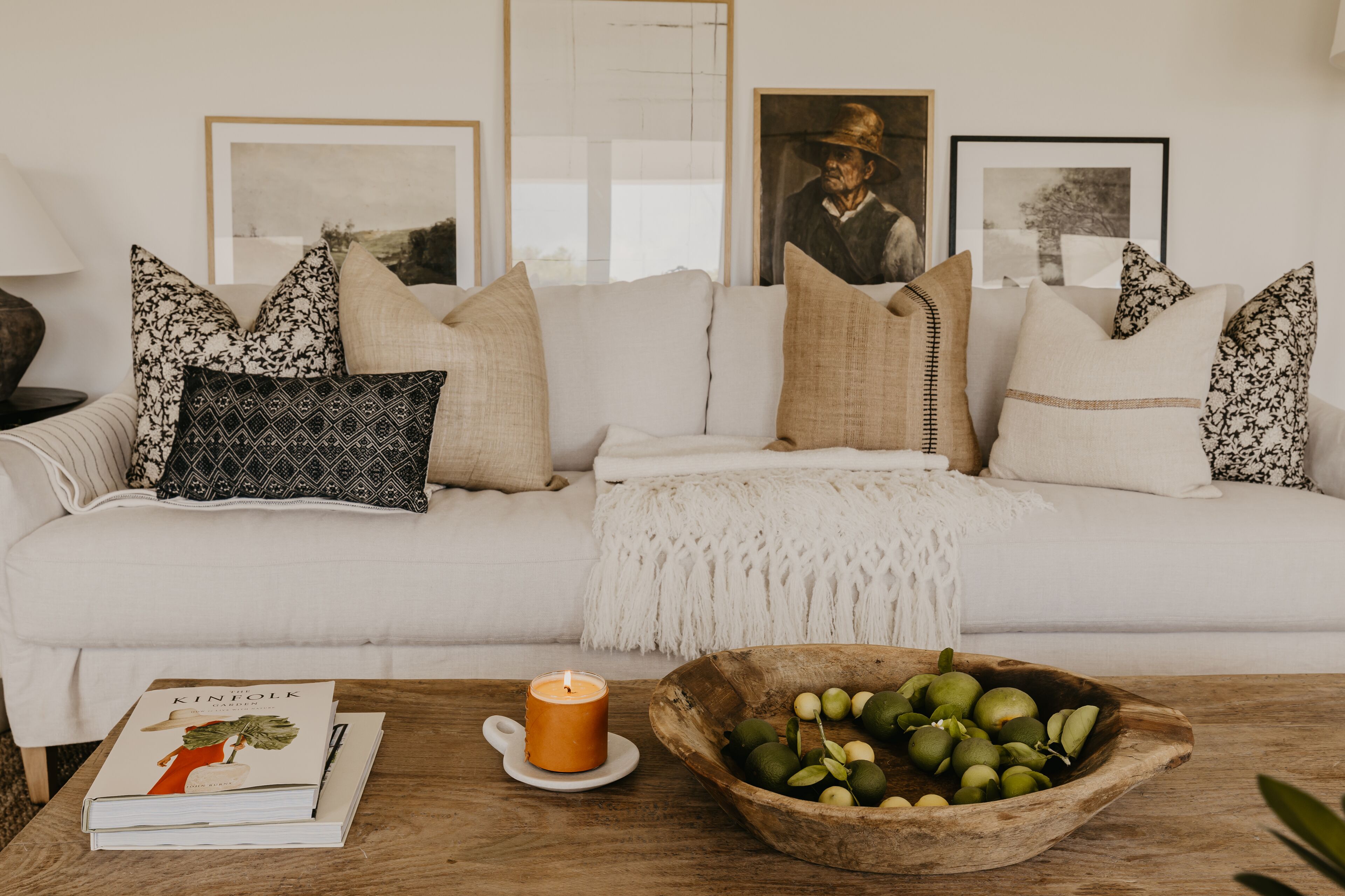 Een woonkamer met een witte bank, een houten bijzettafeltje, een schaal met fruit, een kaars en een boek.
