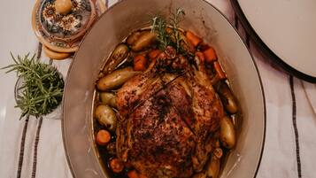A roasted chicken in a pot with vegetables and herbs, placed on a striped tablecloth.