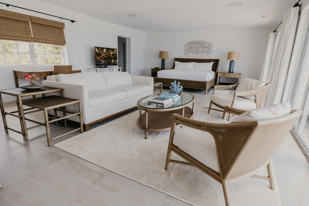 A modern hotel room with a large bed, a sofa, a coffee table, and a chair.