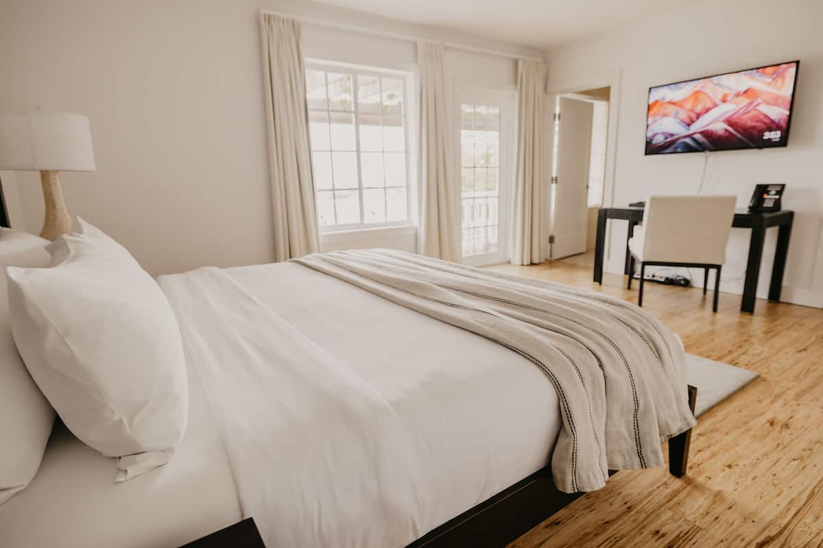 A hotel room with a large bed, a desk, a chair, and a TV on the wall.