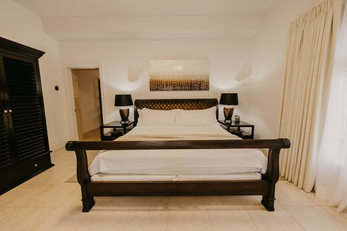 A large bed with a wooden frame, two bedside tables with lamps, a wall-mounted artwork, and a door on the left.