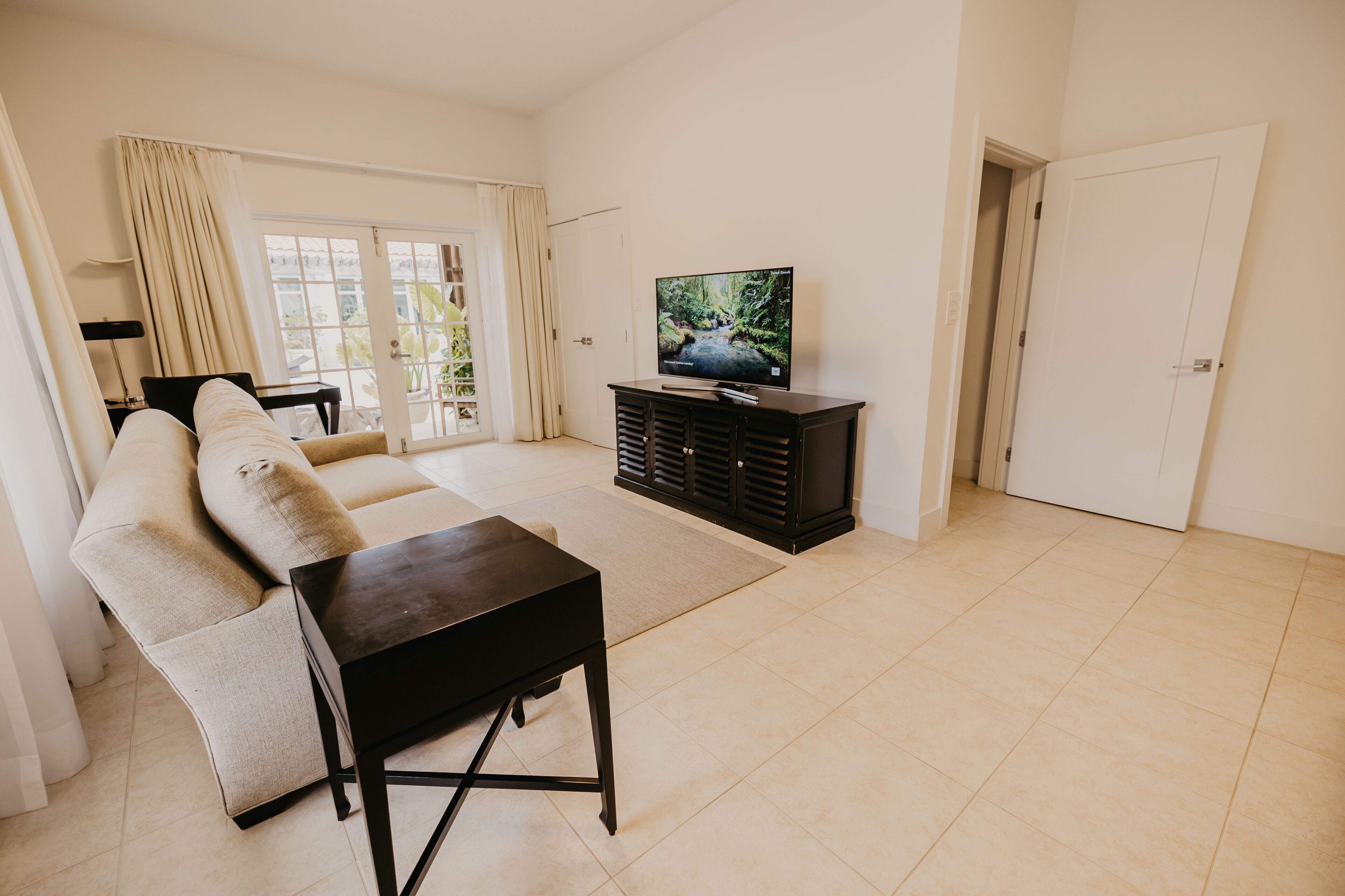 A living room with a sofa, a coffee table, a TV on a stand, and a door.
