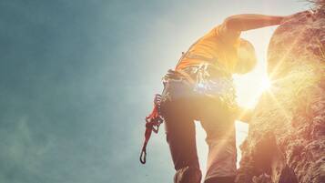 A person climbing a rock with a rope, sun in the background.
