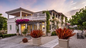 A two-story house with a balcony, potted plants, and a patio area. - Le Soleil d'Or CaymanBrac (West End)