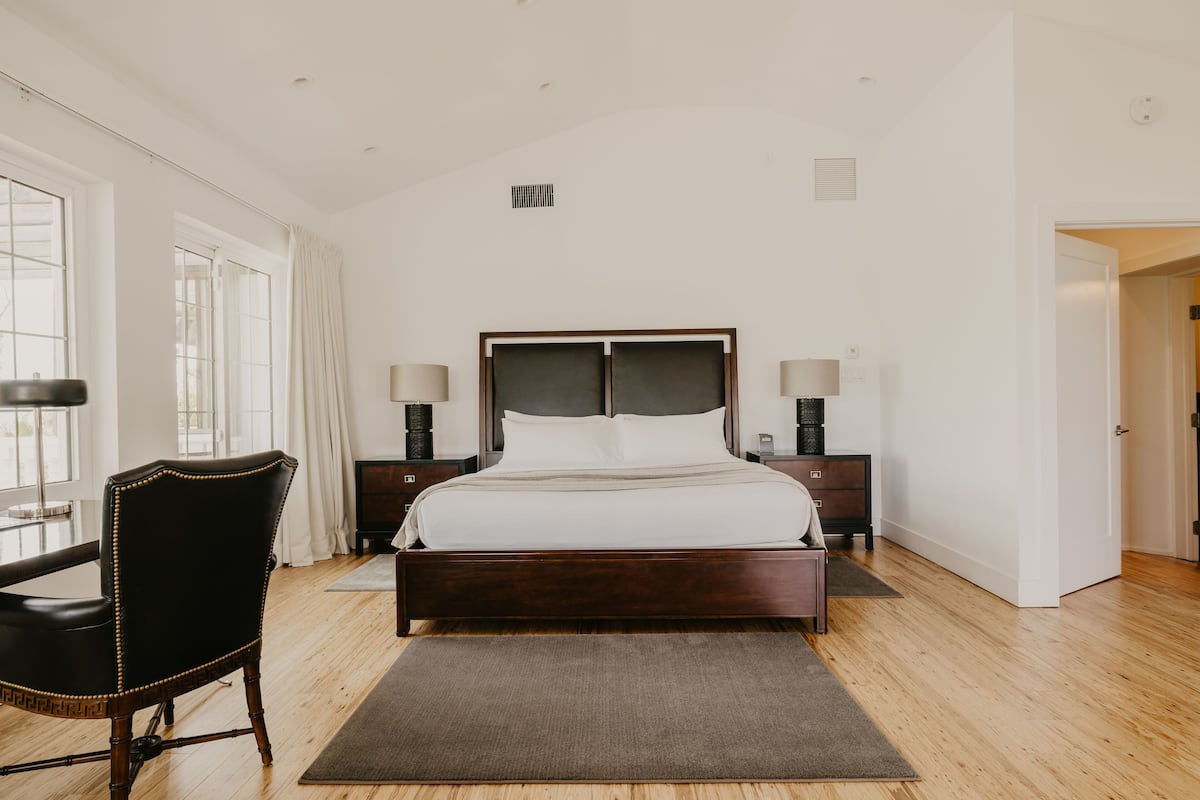 A bedroom with a large bed, a chair, two bedside tables with lamps, and a wooden floor.