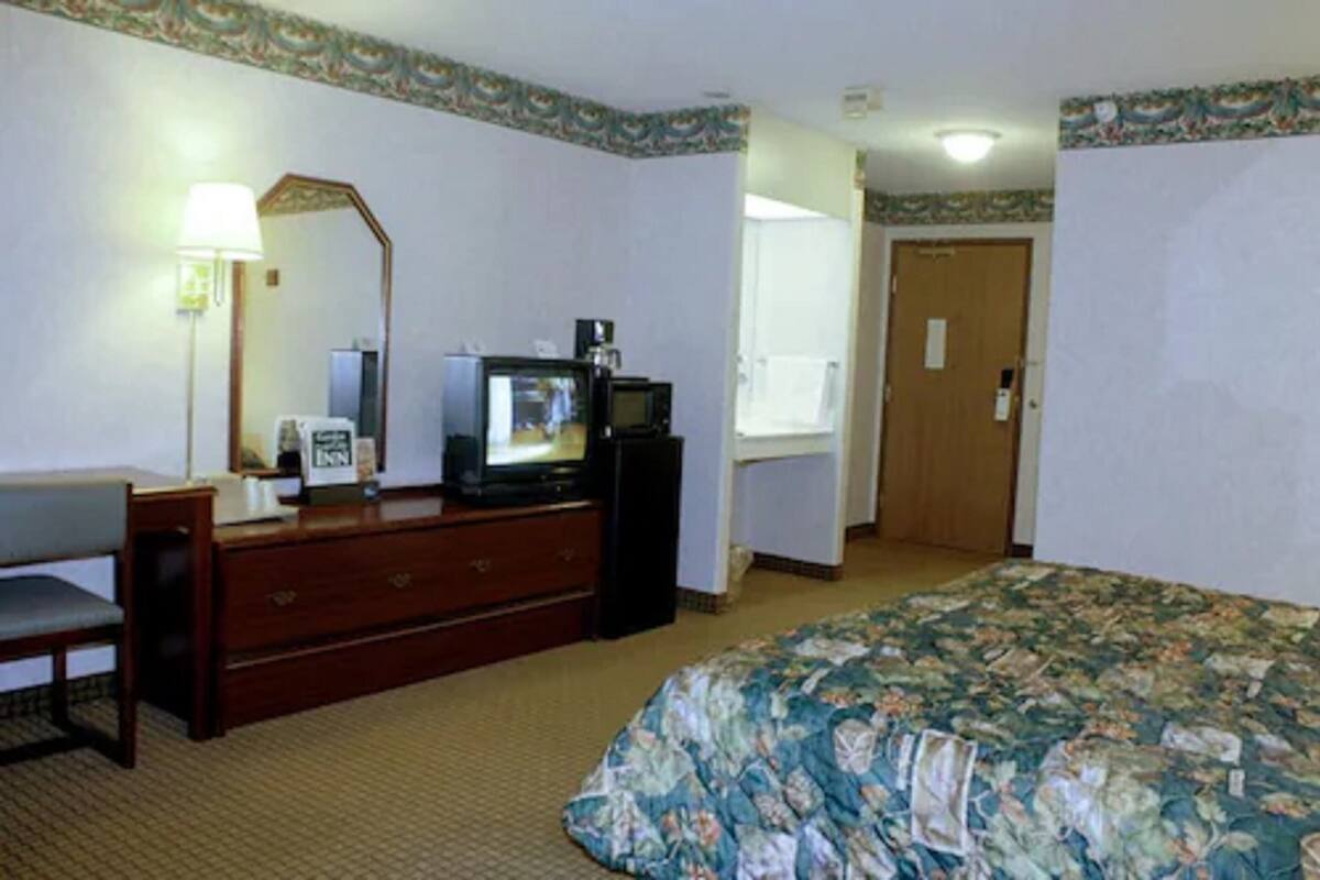 A hotel room with a bed, a desk with a chair, a television, and a dresser.
