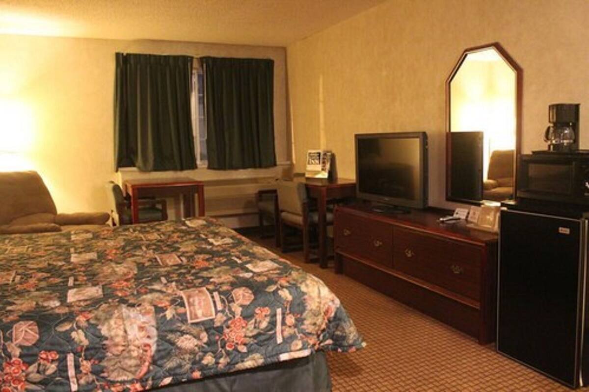A hotel room with a bed, a television, a dresser, a desk, and a window with curtains.