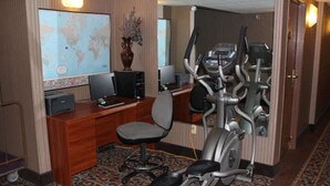 A hotel room with a wooden desk, a computer, an exercise bike, and a map on the wall. - Garden City Inn (Garden City)
