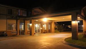 A hotel entrance at night with a covered walkway, a parking area, and a building with multiple windows and doors. - Garden City Inn (Garden City)