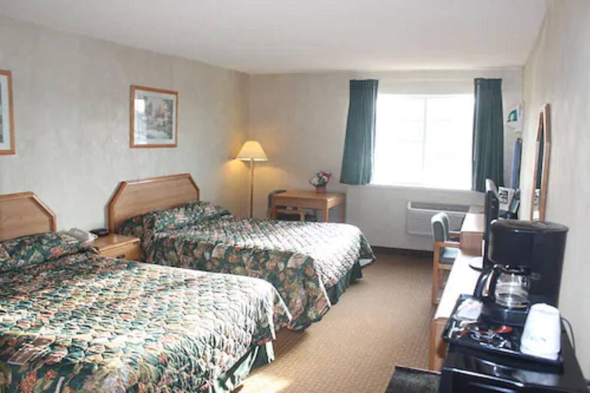 A hotel room with two beds, a desk with a coffee maker, a lamp, and a window with curtains.