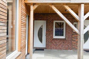 A wooden exterior with a brick wall and a white door. - Vacation apartment Ahoi in Schillig, walking distance to the beach, WLAN & Sky (Wangerland)