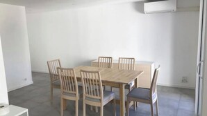 A dining area with a wooden table and six chairs, a white wall, and a ceiling-mounted air conditioning unit. - Apartment 300 m from Cannes beach (Cannes)