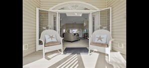 A spacious room with two white wicker chairs with star-shaped cushions, a central seating area with a sofa and coffee table, and a view into the living area.