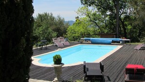 A rectangular swimming pool with a wooden deck surrounding it, equipped with lounge chairs and a small table. - Barjac Villa Pastis - Self-catering cottage with swimming pool and view of the Cevennes mountains (Barjac)