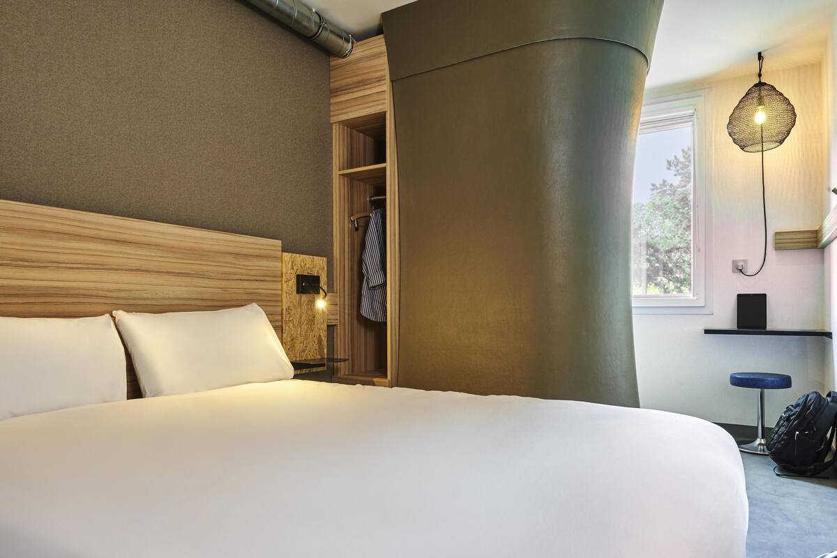 Hotelkamer met een groot bed, een houten hoofdbord, een inbouwkast, een hanglamp en een raam met uitzicht.