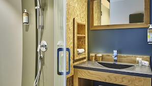 Een badkamer met een glazen douchecabine, een houten wastafelmeubel met een wastafel, een spiegel en een plank met handdoeken.