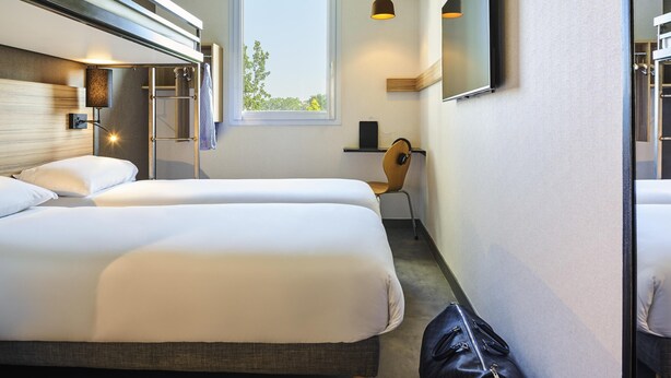 Hotelkamer met twee bedden, een bureau, een stoel, een televisie en een raam met uitzicht op bomen.