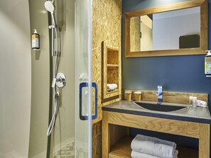 Une salle de bain avec une douche à parois de verre, un meuble-lavabo en bois avec un évier, un miroir et une étagère avec des serviettes.
