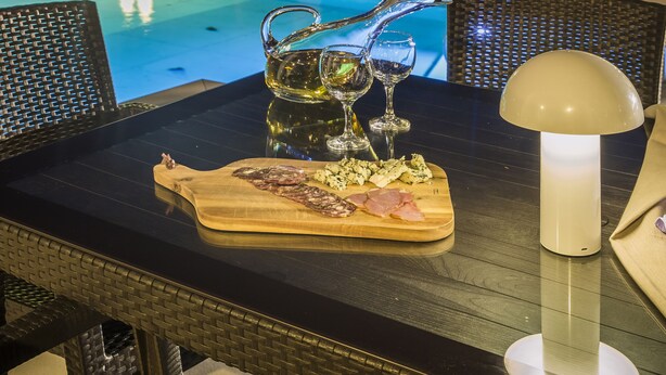 Ein Essbereich am Pool mit einem Tisch für zwei Personen, einer Holzplatte mit Essen und einer Lampe.