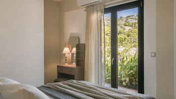 A bedroom with a bed, bedside table with lamps, a dresser, and a sliding glass door leading to a garden.
